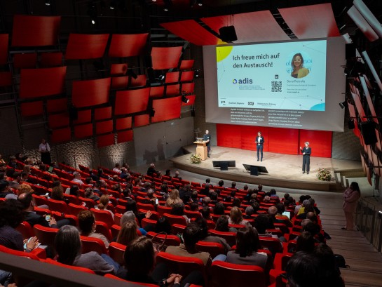 Auditorium im Zentrum Paul Klee von oben fotografiert. Zuschauer sitzen auf roten Sitzen und verfolgen gespannt die Präsentationen.